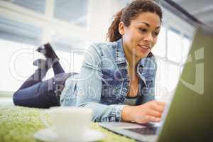 Businesswoman lying on carpet while using laptop