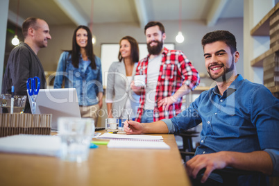 Confident creative businessman with colleagues standing by table