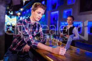 Man using laptop at bar counter with bartender working