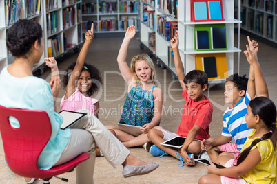 Teacher sitting on chair by children raising hands