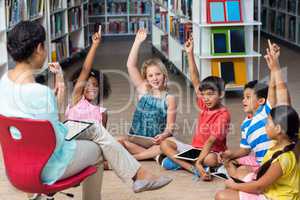Teacher sitting on chair by children raising hands