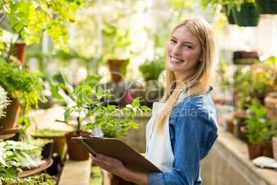 Female gardener holding clipboard while examining plants