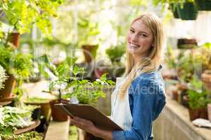 Female gardener holding clipboard while examining plants