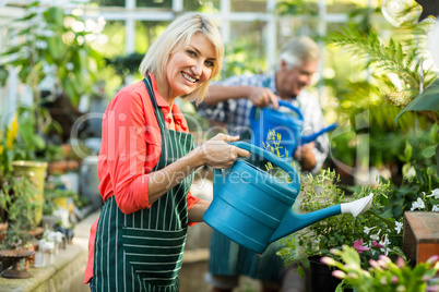 Woman watering plants with man at greenhouse