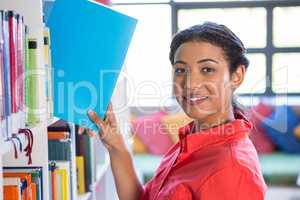 Smiling teacher removing book from bookshelf at library