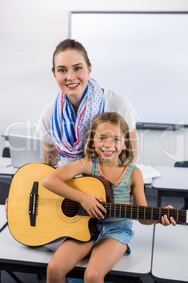 Portrait of teacher assisting girl to play guitar in classroom
