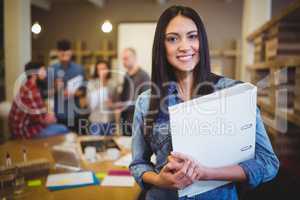 Confident businesswoman holding file while colleagues in backgro