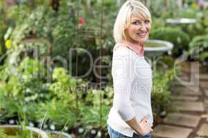 Happy mature woman with hand on hip at greenhouse