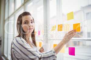 Portrait of businesswoman touching adhesive notes on window whil