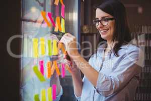 Creative businesswoman sticking adhesive notes to glass in offic