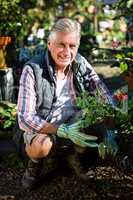 Portrait of happy gardener crouching with potted plants at garde