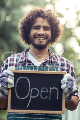 Smiling male gardener holding open sign placard