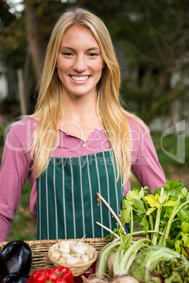 Portrait of happy gardener with fresh vegetables in basket at ga