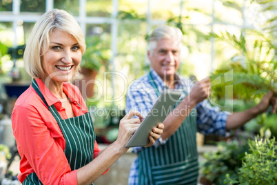 Woman using digital tablet while man working at greenhouse