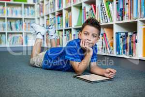 Boy lying with digital tablet in school library