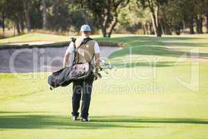 Rear view of sportsman walking with his golf bag