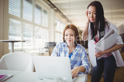 Female colleagues working on laptop in creative office