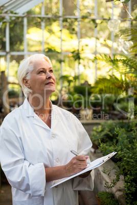 Female scientist writing in clipboard while examining plants