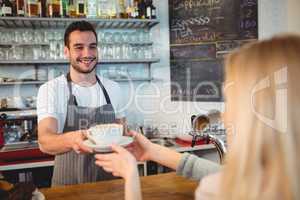 Happy barista serving coffee to woman at cafe