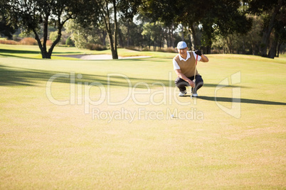 Distant view of golfer crouching and looking his ball