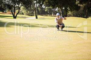 Distant view of golfer crouching and looking his ball