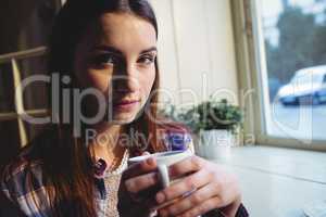 Portrait of beautiful woman sitting with coffee by window at caf