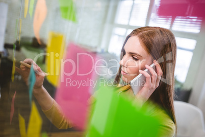 Businesswoman talking on phone white writing on sticky notes
