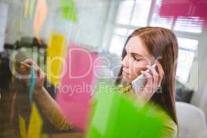 Businesswoman talking on phone white writing on sticky notes