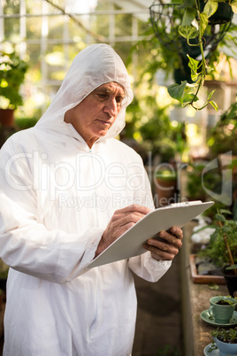 Male scientist writing on clipboard while examining plants