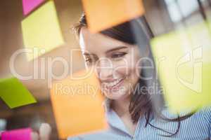 Businesswoman looking at sticky notes stuck to glass