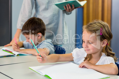 Schoolchildren writing on book against teacher