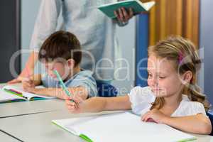 Schoolchildren writing on book against teacher