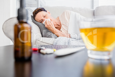 Woman sneezing with herbal tea and medicine on foreground