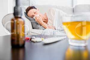 Woman sneezing with herbal tea and medicine on foreground