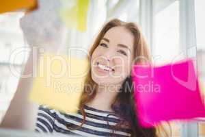 Smiling businesswoman touching adhesive notes in creative office