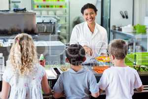 Cheerful woman serving food to schoolchildren