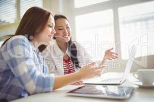 Female colleagues discussing on laptop in creative office