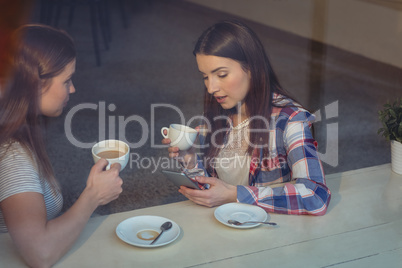 Beautiful woman using cellphone with friend at cafe