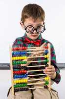 Cute boy playing with abacus against whiteboard in classroom