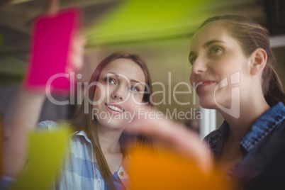 Businesswomen looking at adhesive notes on window in office