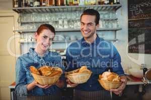 Portrait of cheerful baristas offering breads at coffee shop