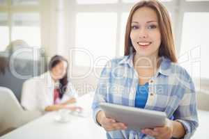 Businesswoman holding digital tablet with colleague in backgroun