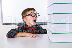 Surprised boy by stacked books in classroom