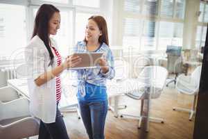 Young female colleagues discussing with digital tablet in office