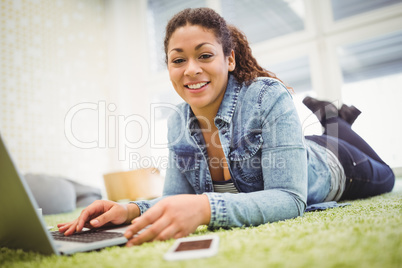 Portrait of businesswoman lying on carpet while using laptop