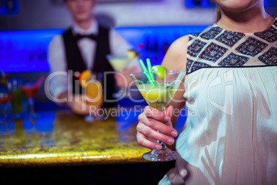 Woman with cocktail glass standing by bartender