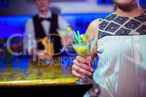 Woman with cocktail glass standing by bartender