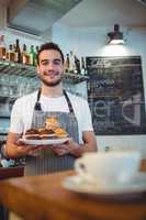Portrait of confident waiter with cupcakes at coffee house