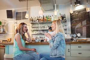 Happy friends talking at counter in coffee shop