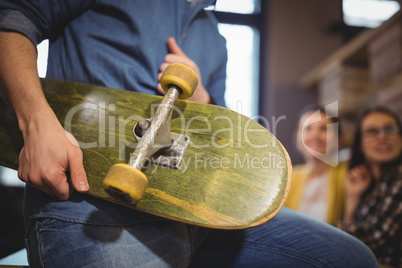 Businessman holding skateboard while sitting in creative office